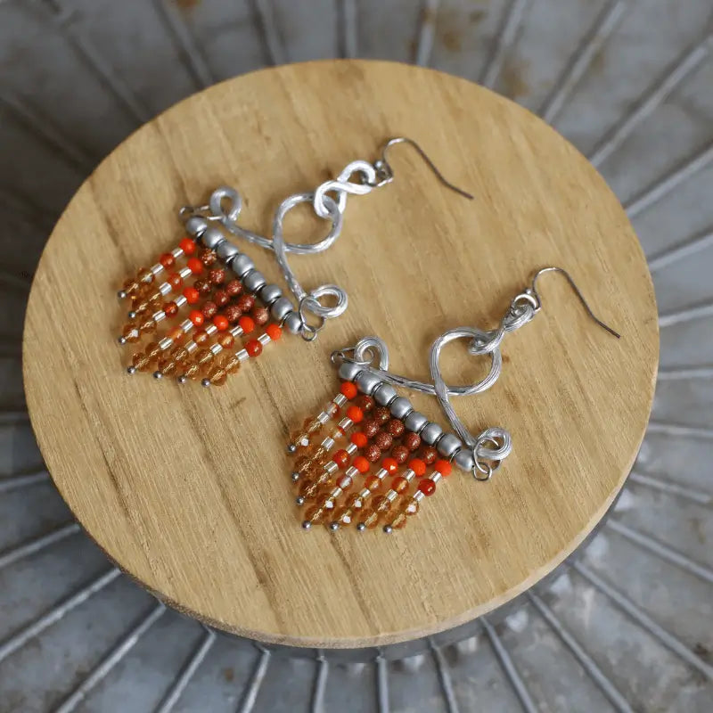 fringe seed beads chandelier hook earrings in brown orange color laying on a wooden circle
