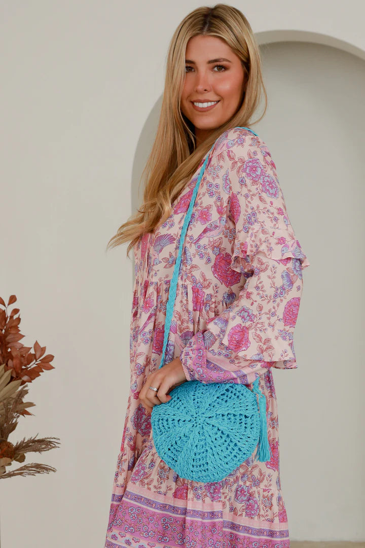 woman carrying a turquoise round straw crossbody bag with tassel