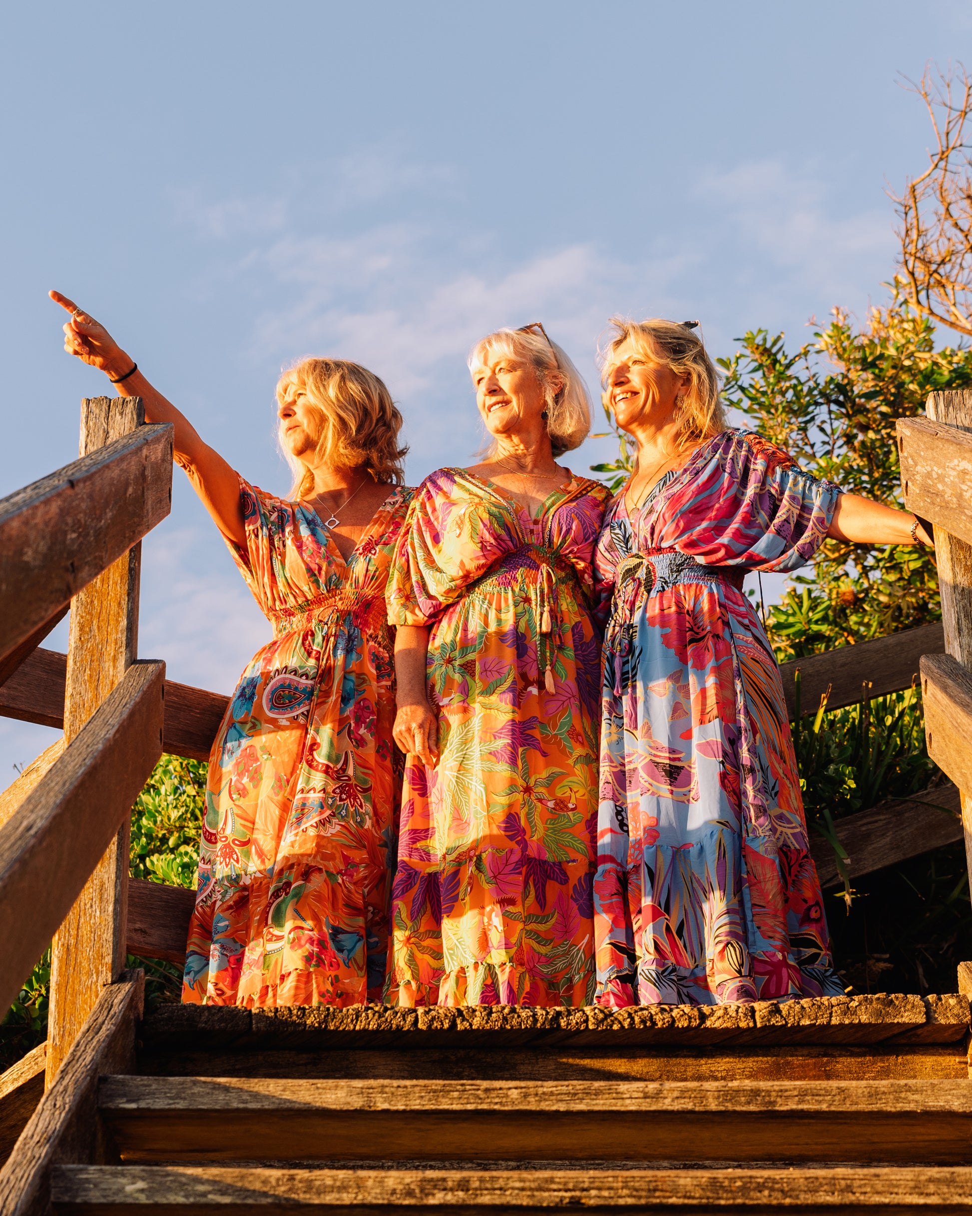 three women standing on the stairs wearing a floral silk maxi dress
