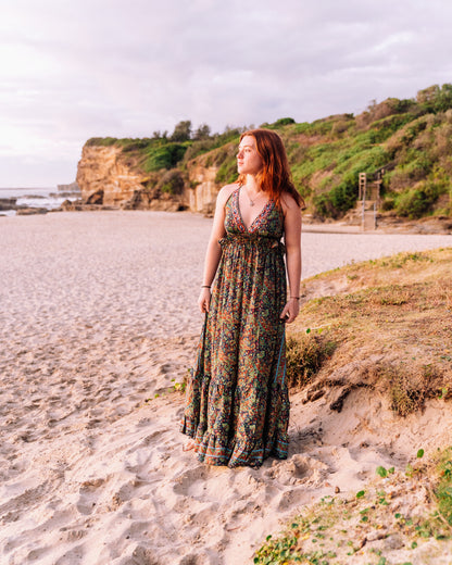 woman at the beach wearing a halter neck tiered maxi dress in paisley print