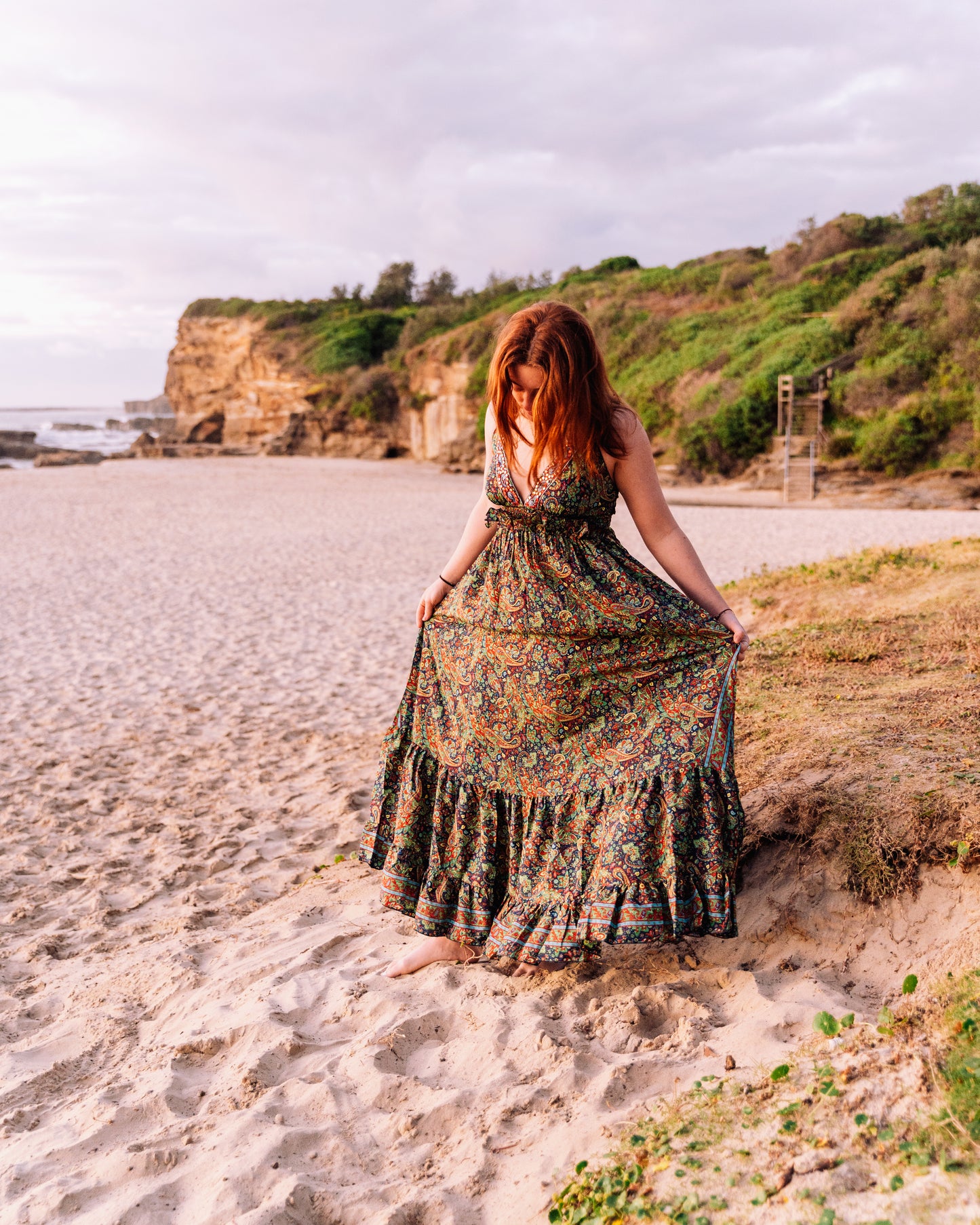 woman at the beach wearing a halter neck tiered maxi dress in paisley print