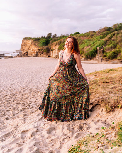 woman at the beach wearing a halter neck tiered maxi dress in paisley print