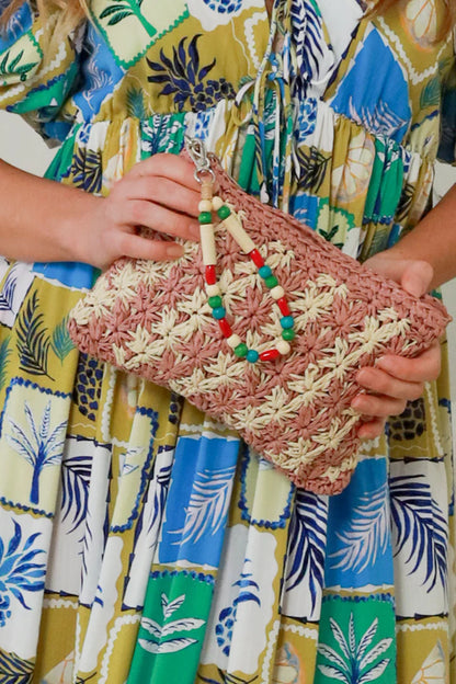 woman carrying an old rose natural straw woven clutch with colorful beaded wristlet 