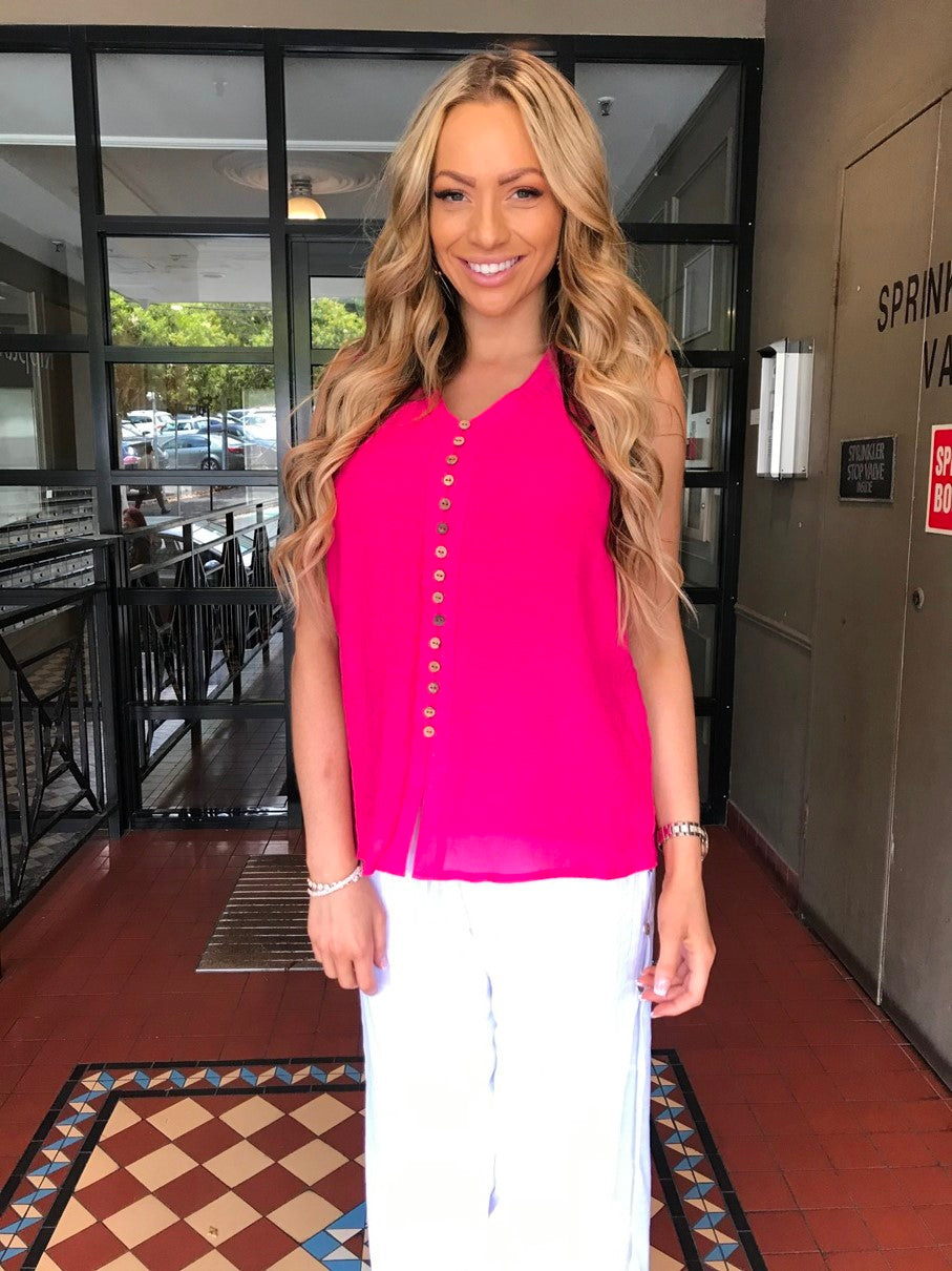 woman wearing a coconut shell button sleeveless chiffon top in hot pink