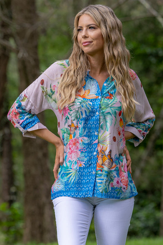 woman standing wearing a tropical floral butterfly print long sleeve button down shirt - light pink and blue
