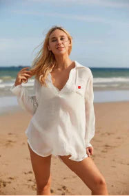 woman on a beach shore wearing white oversized collared beach shirt