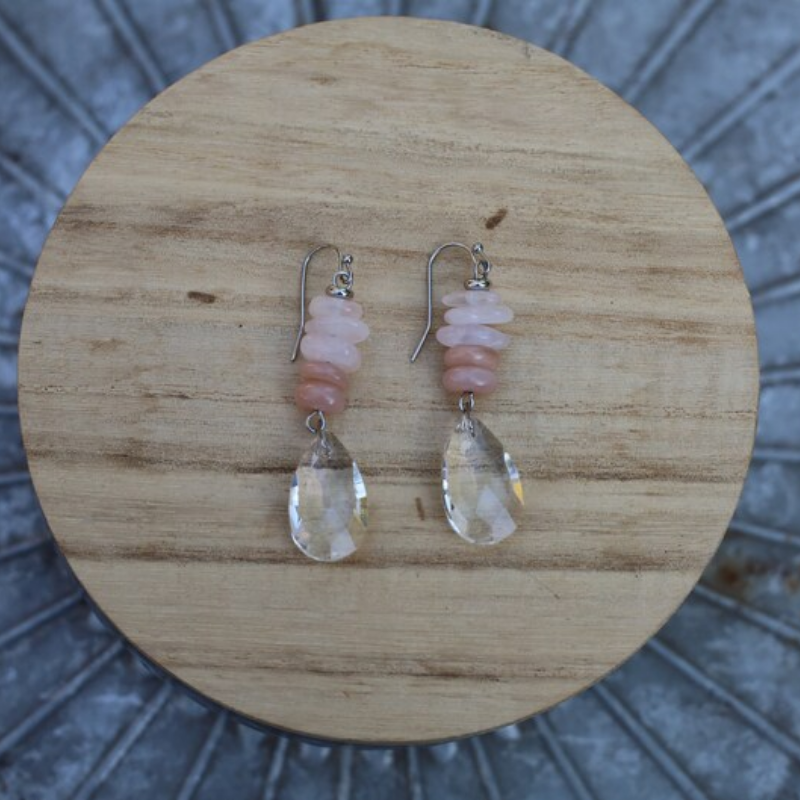 multiple stone stack with crystal teardrop dangling hook earrings laying on a wooden circle