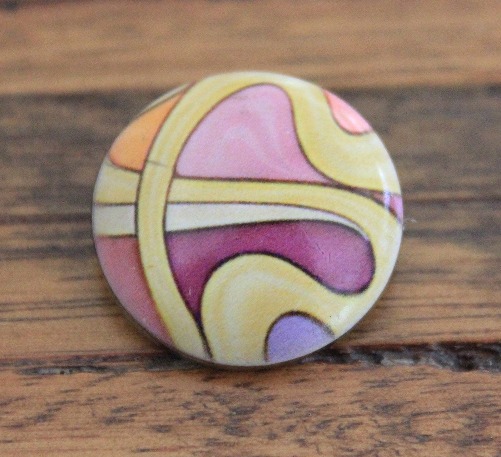 yellow swirl pattern on a pink painted stone button