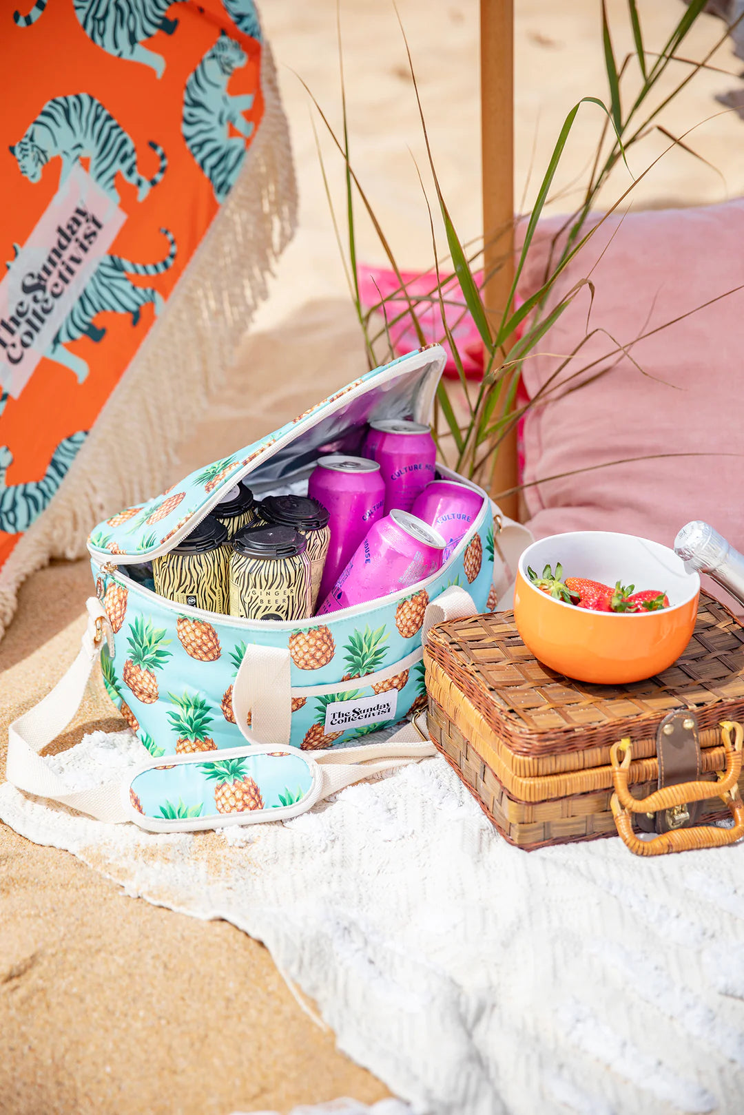 Collapsible Cooler Bag in Pineapple Print by The Sunday Collectivist - PACIFICA 32cm X 20cm X 17cm with beer cans inside laying on a beach sand with towel