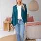 woman wearing white top layered with emerald freez cape shrug and denim jeans and white sneakers