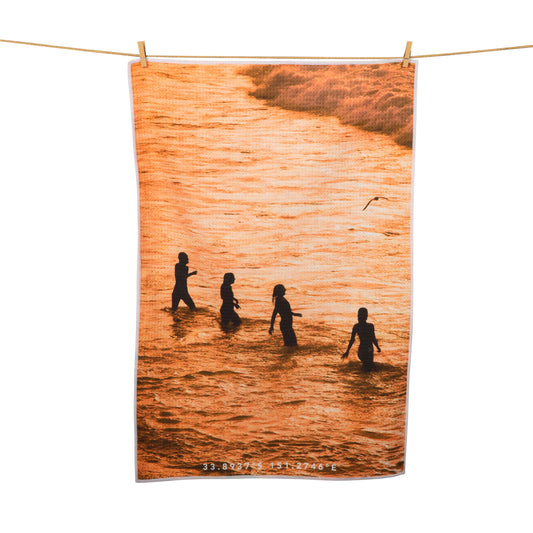four people at the beach sunset print tea towel hanging